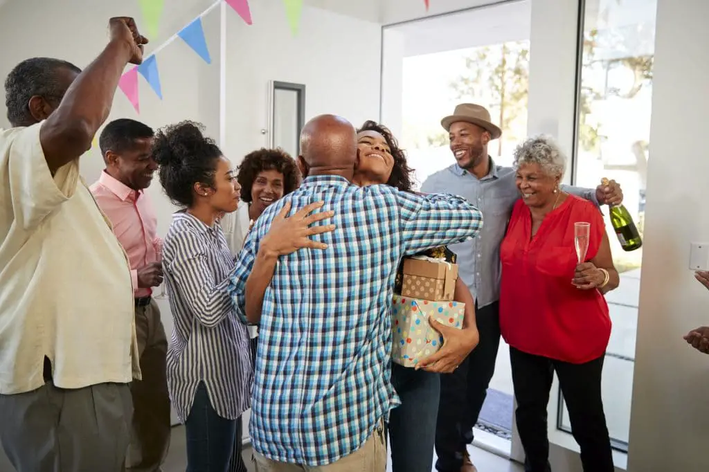 Black grandparents welcoming guests to their house for a family party