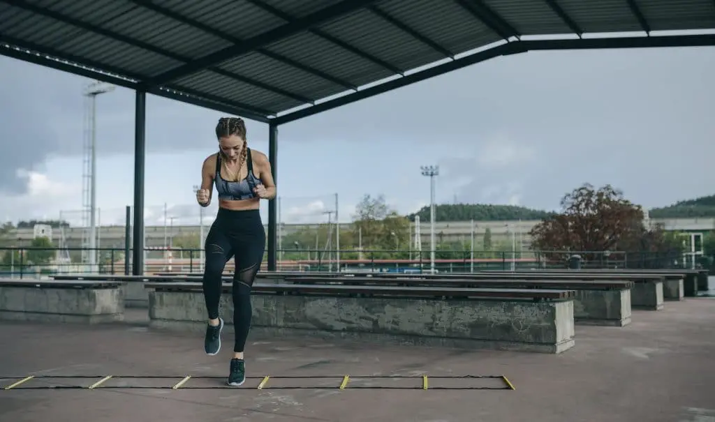 Sportswoman jumping on an agility ladder