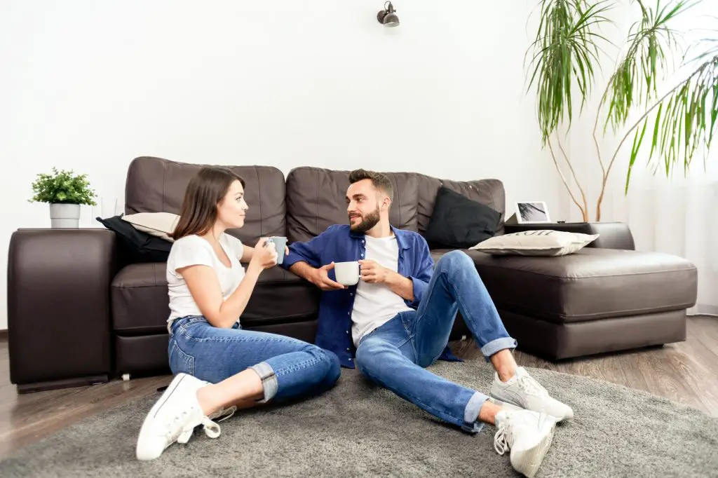 Content young couple in jeans and white shoes sitting on carpet