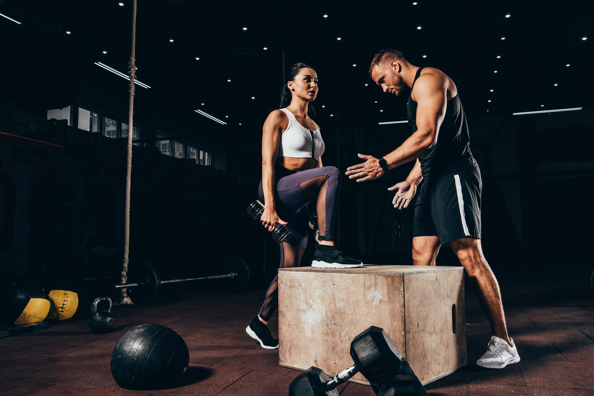 fit woman exercising with trainer on cube in dark gym