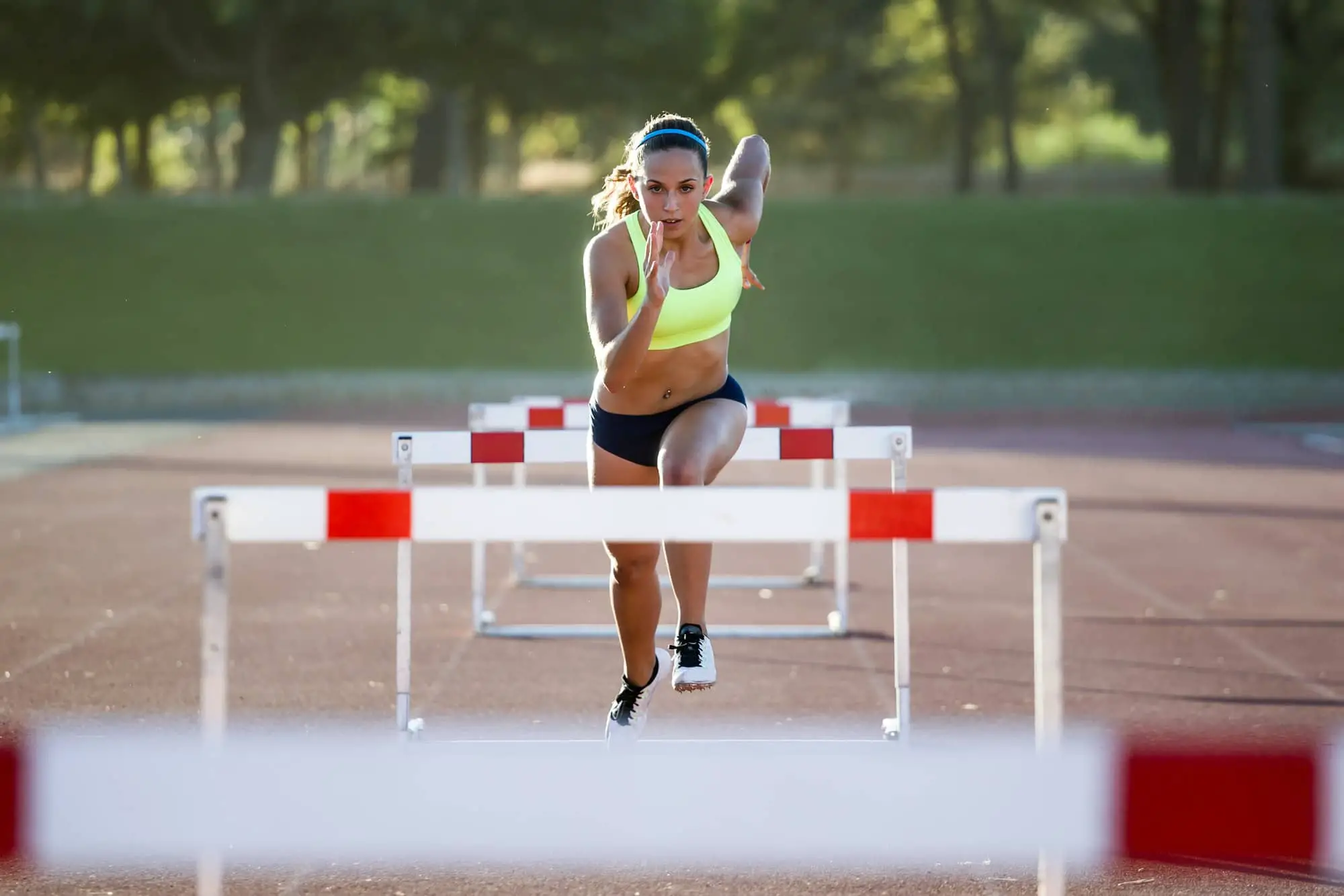 Young athlete jumping over a hurdle during training on race trac