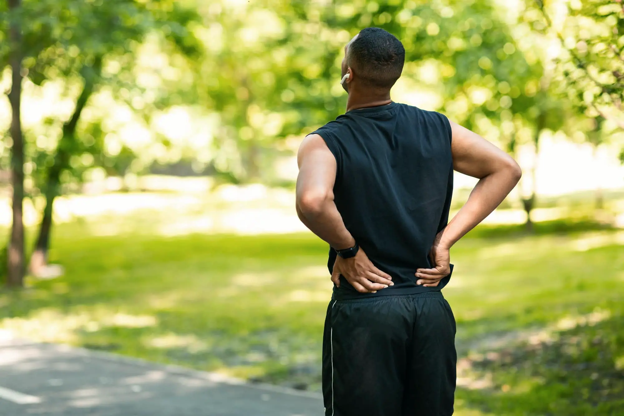 Millennial guy in sportswear suffering from back pain wgilejogging at park, empty space