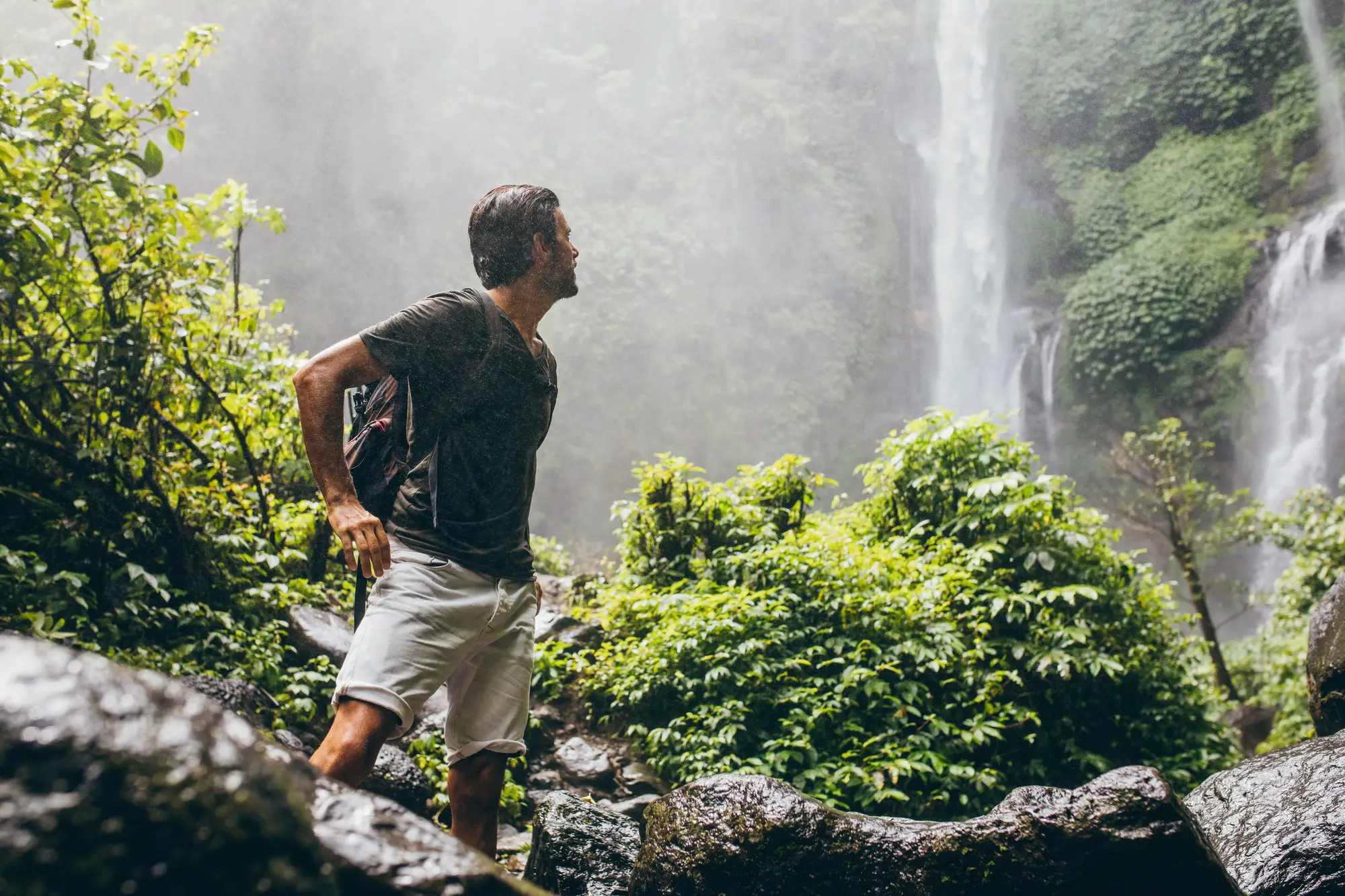 Male hiker near waterfall during rain