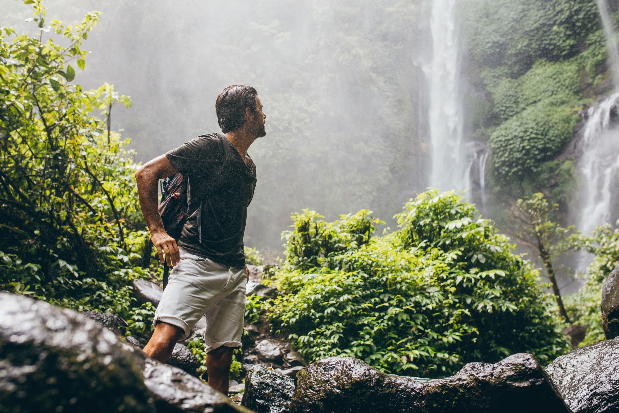 Male hiker near waterfall during rain