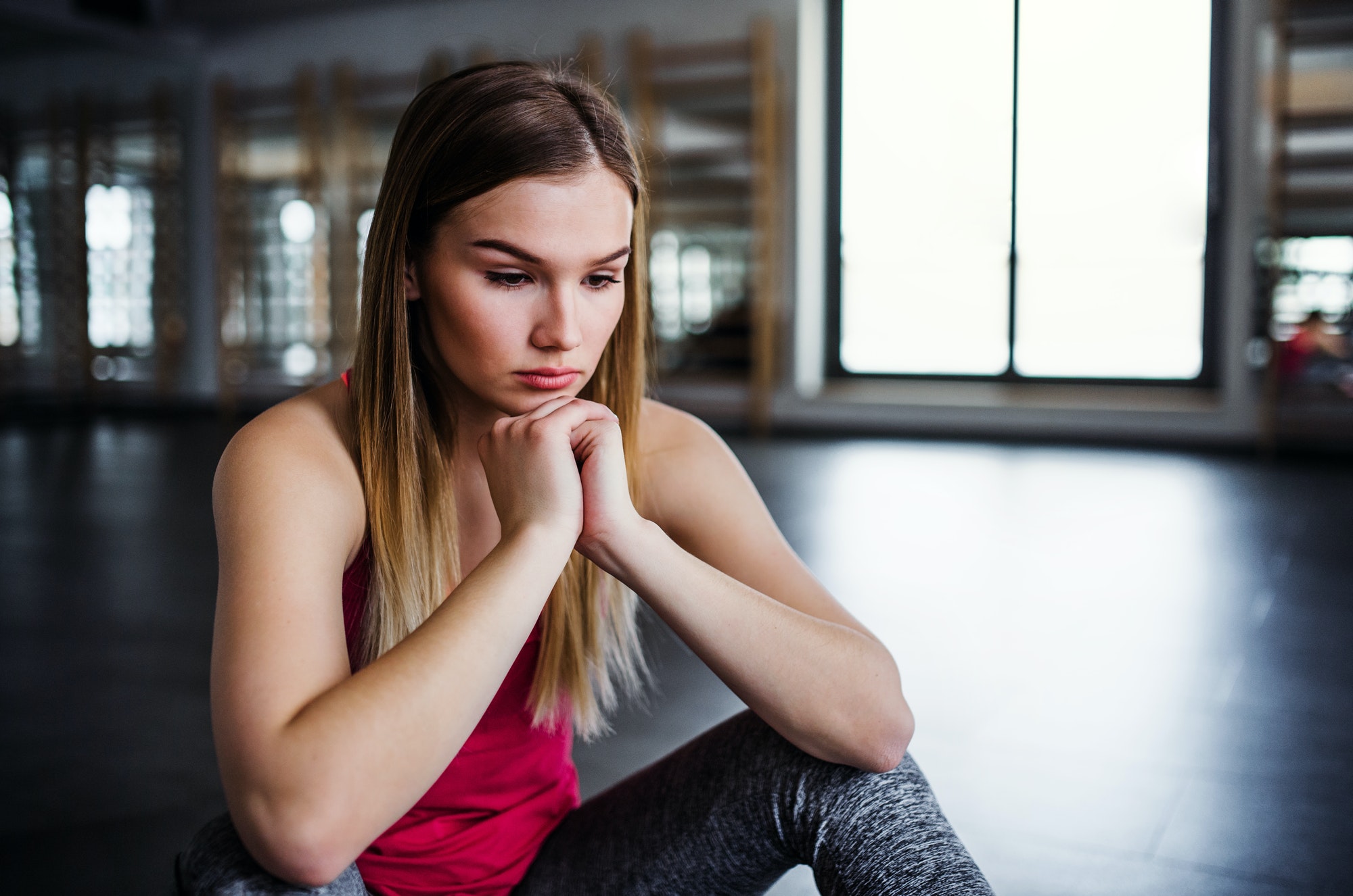 A portrait of young sad and frustrated girl or woman sitting in a gym.