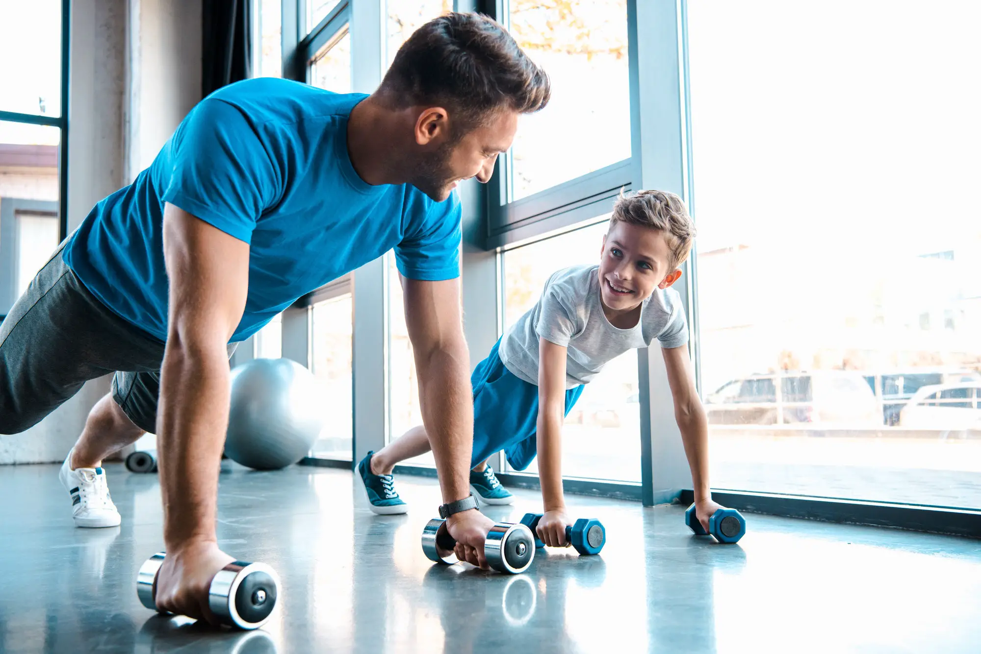 happy father looking at cheerful son and exercising with dumbbells