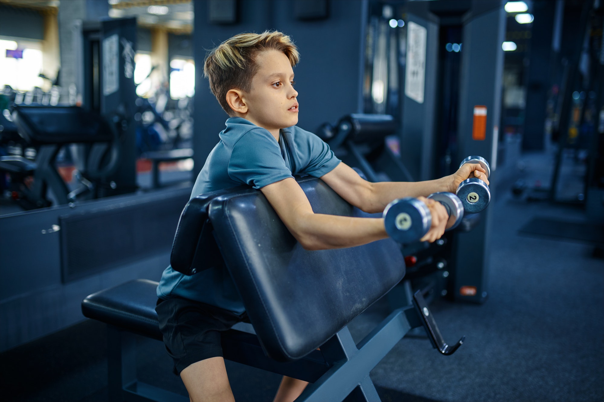 Teenager doing exercise with dumbbells in gym