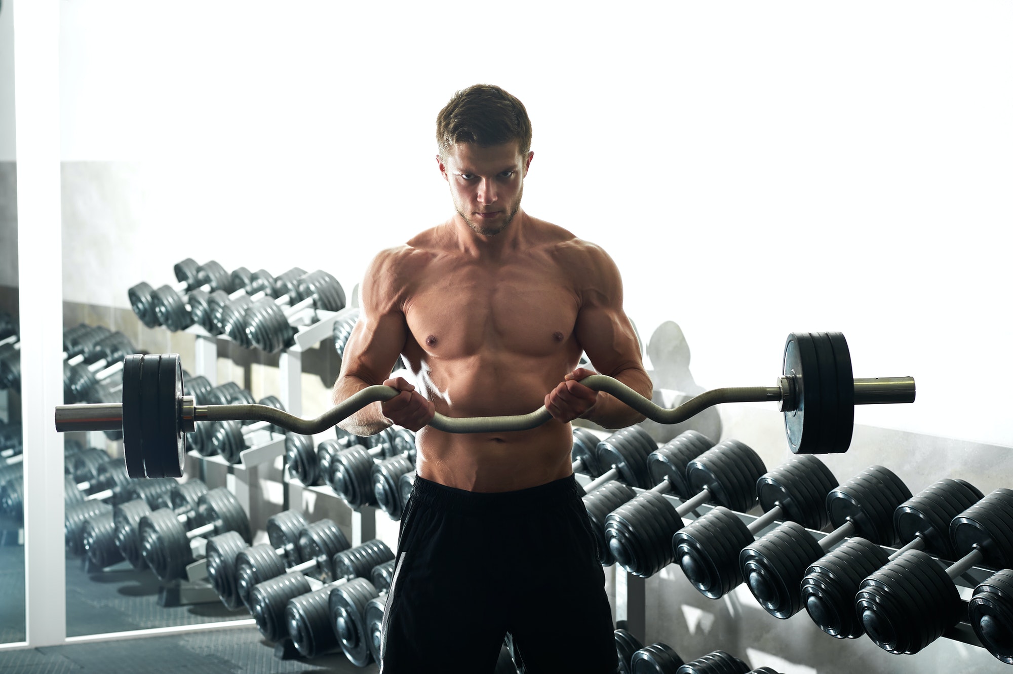 Young fitness man with muscular body exercising with ez curl bar