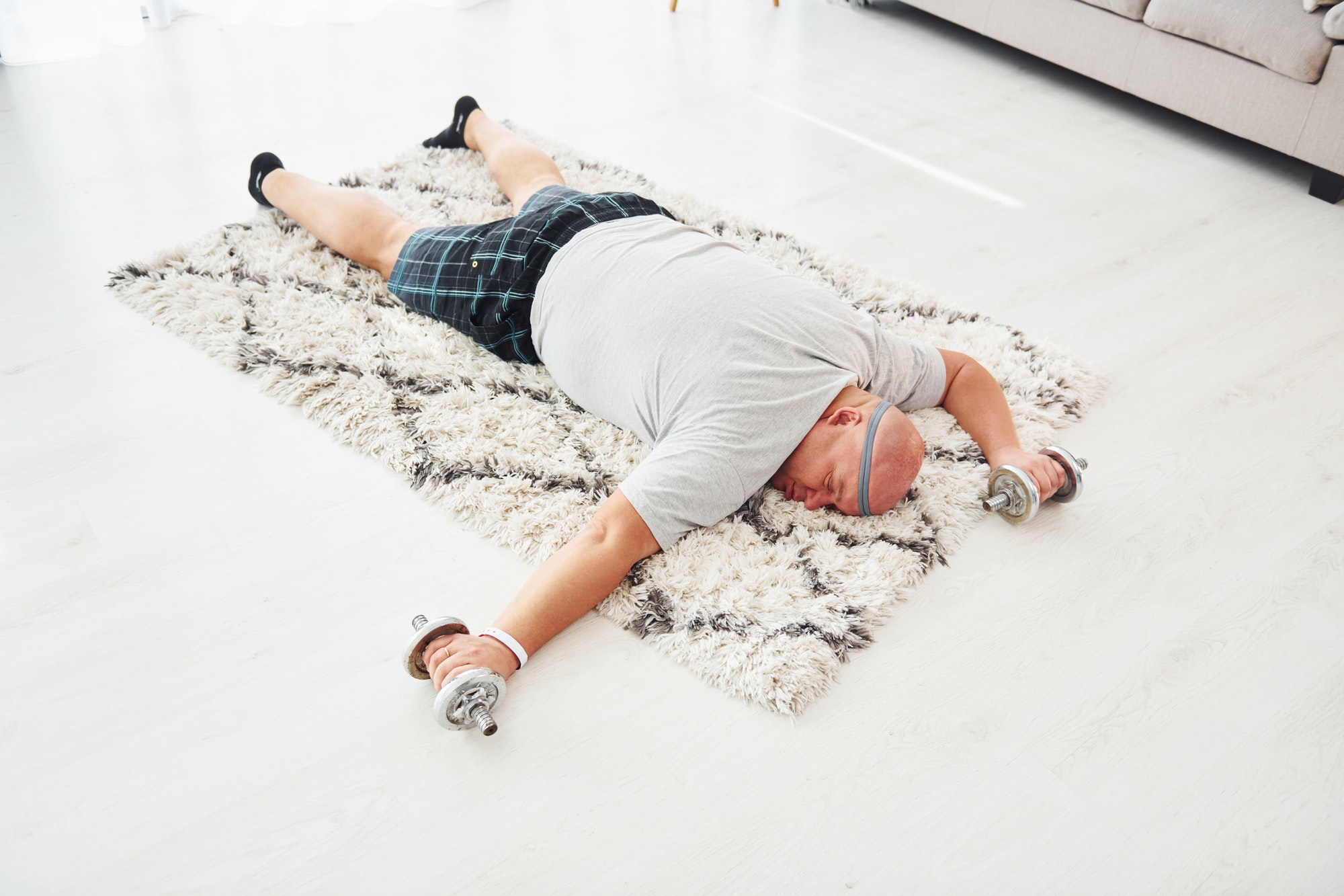 With dumbbells in hands. Funny overweight man in casual clothes is indoors at home