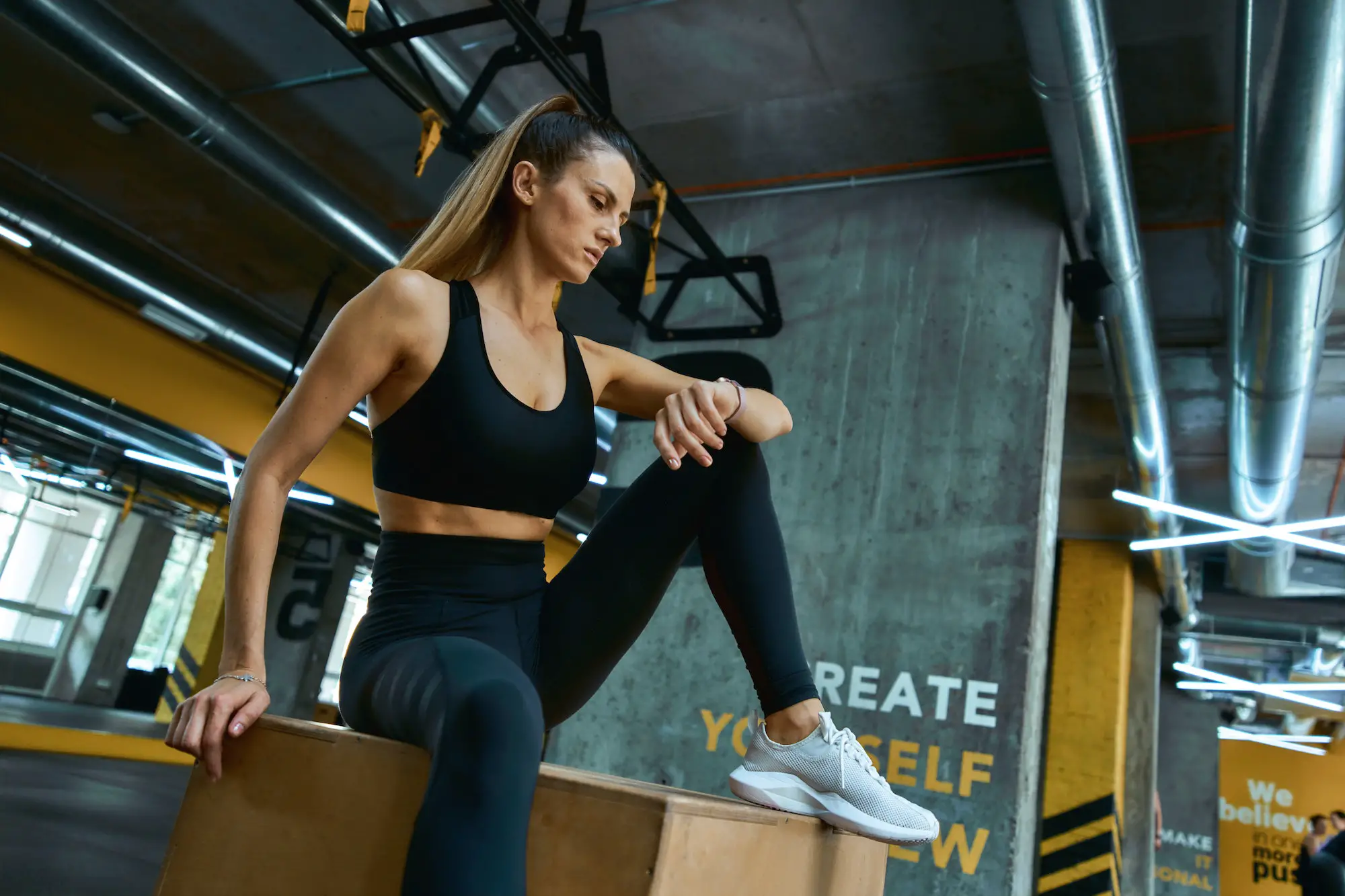 Checking fitness results. Young beautiful athletic girl in sportswear sitting on wooden crossfit