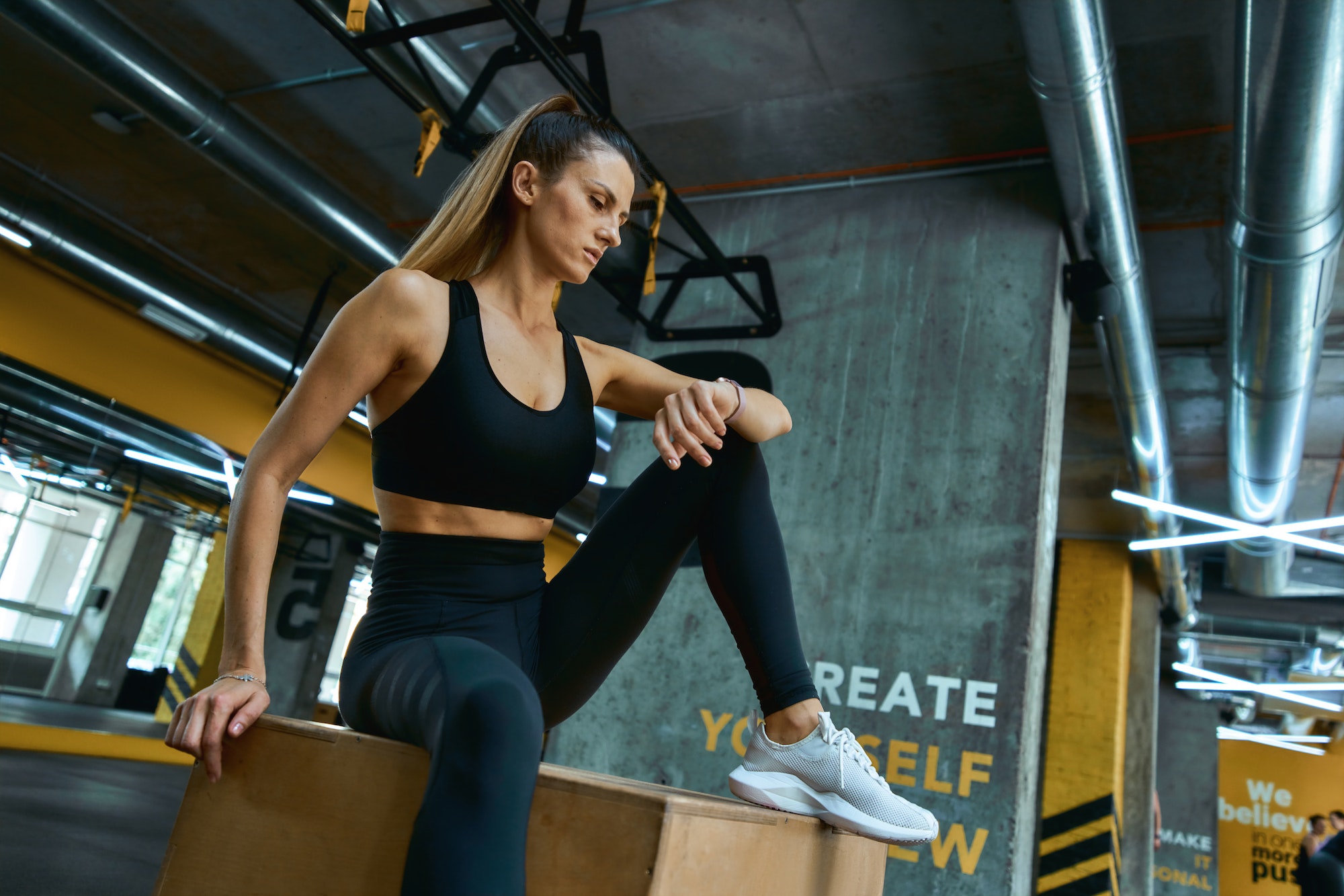 Checking fitness results. Young beautiful athletic girl in sportswear sitting on wooden crossfit