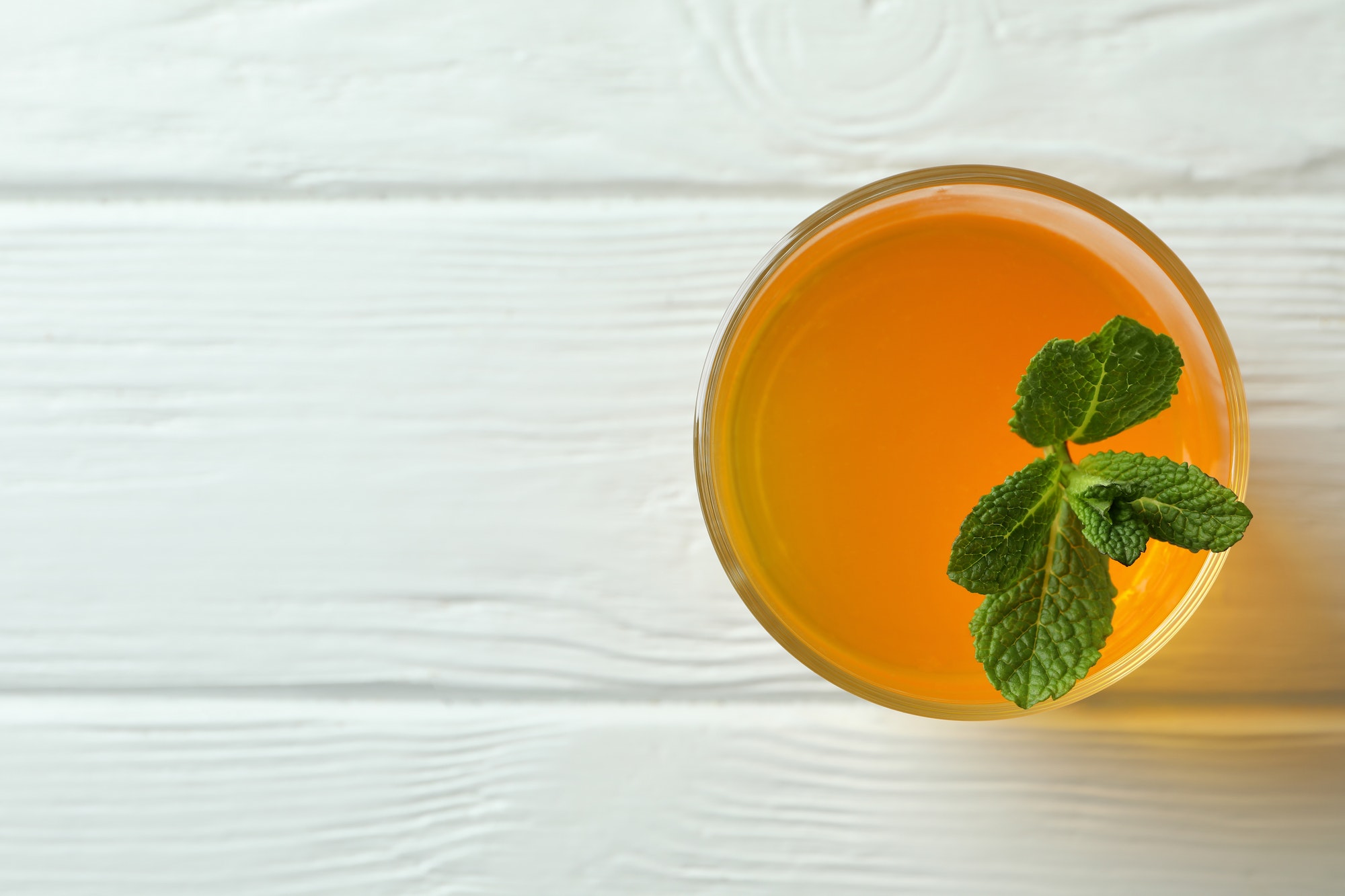 Glass of orange jelly with mint on white wooden table