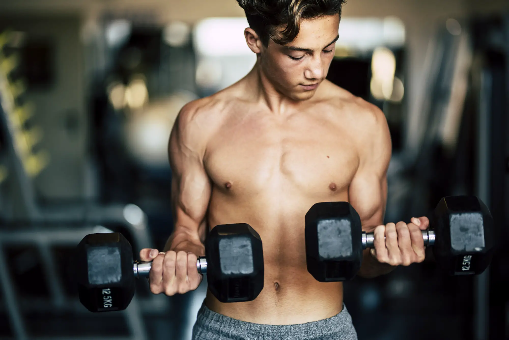 one teenager alone at the gym training and lifting a dumbbels - strong and with muscles man