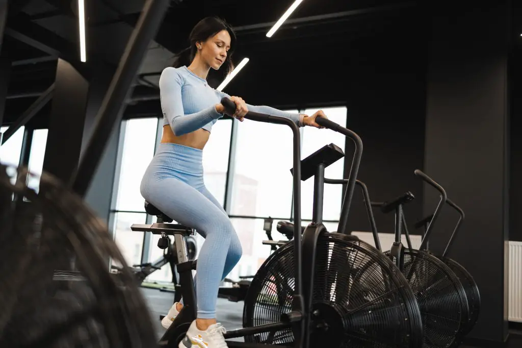 Pretty woman in crossfit gym using exercise bike for cardio workout. Sport girl on air bike