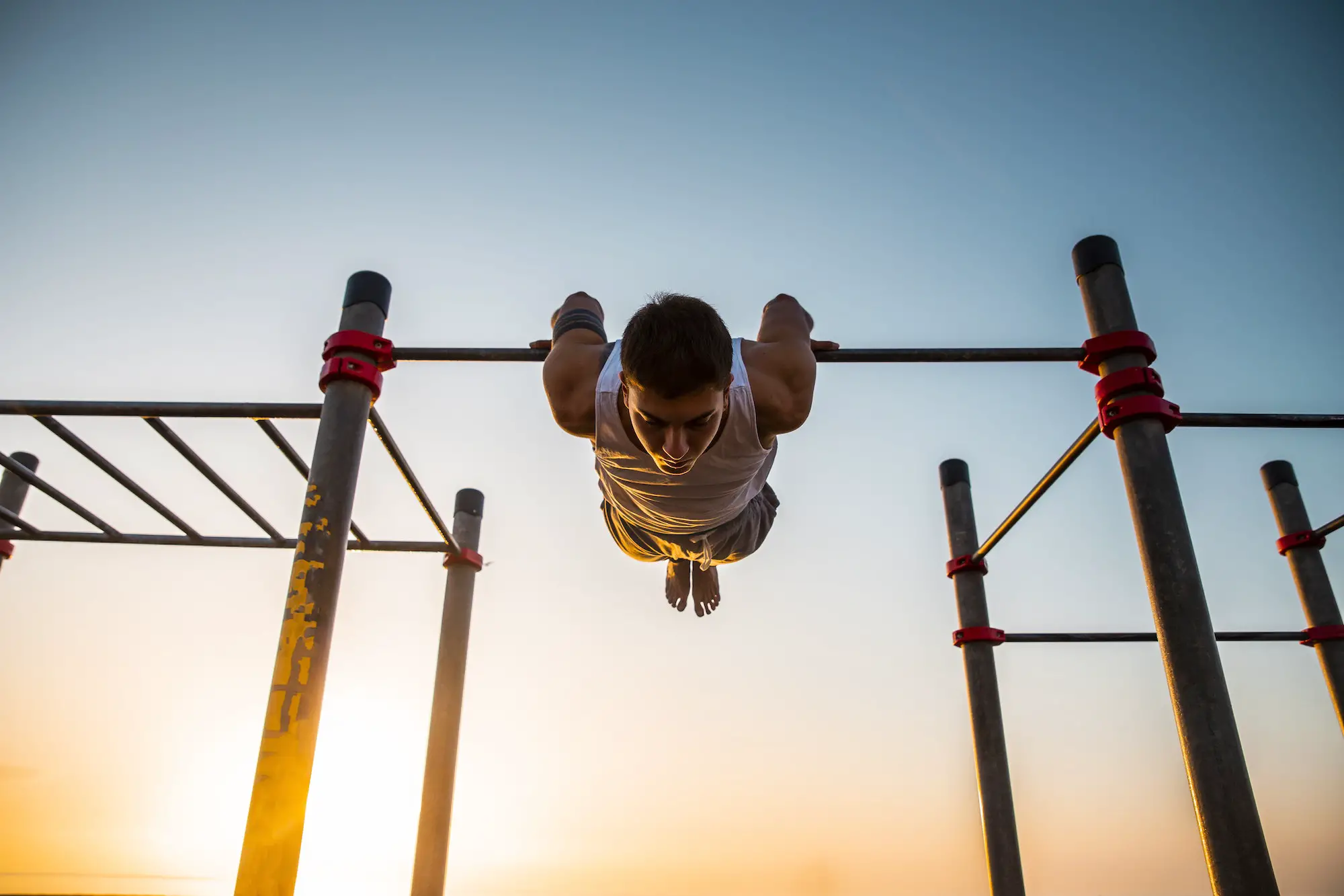 Young man practicing calisthenics at an outdoor gym at sunrise